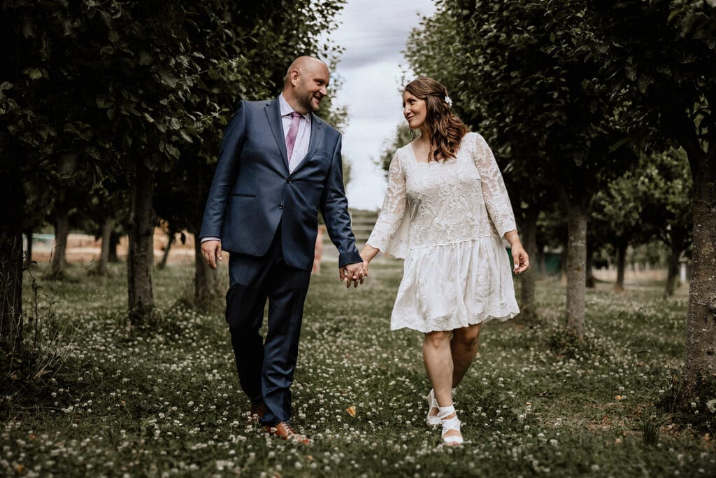Glessener Mühlenhof Bergheim Hochzeitsfotograf - Hochzeitspaar hält Händchen und geht Baumallee entlang