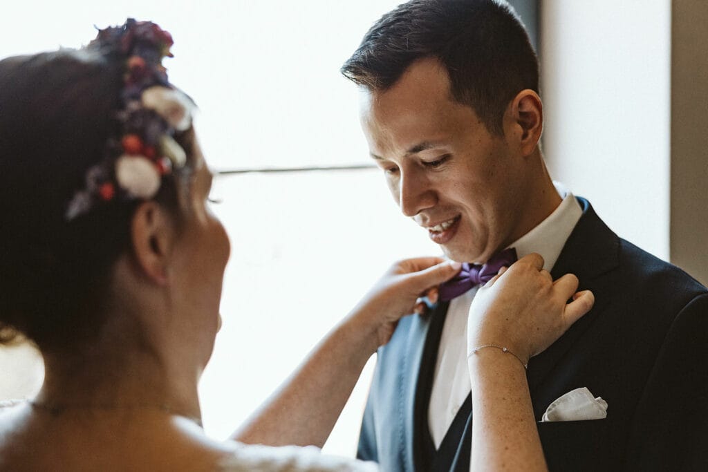 Herrenhaus Cromford Ratingen 25hours Hotel Düsseldorf Hochzeitsfotograf - Braut richtet Fliege des Bräutigams First Look