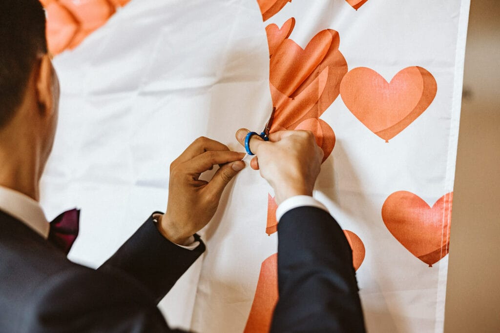 Herrenhaus Cromford Ratingen 25hours Hotel Düsseldorf Hochzeitsfotograf - Bräutigam schneidet mit kleiner Schere Stoff durch