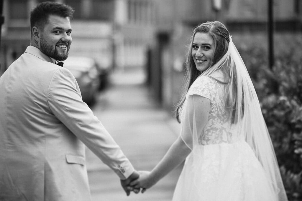 St. Lambertus Mettmann Trüffelschwein Hilden Hochzeitsfotograf - Braut und Bräutigam gehen Hand in Hand und schauen rückwärts in die Kamera