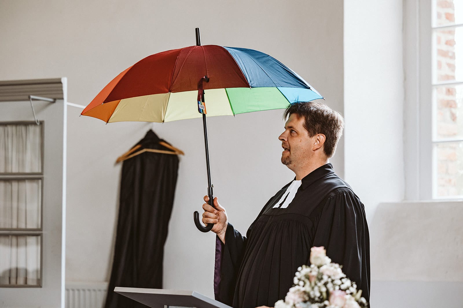 Schlosskapelle Diersfordt Wesel Schloss Diersfordt Wesel Hochzeitsfotograf - Pfarrer hält Schirm in Regenbogenfarben in der Hand um die Vielfalt der Liebe zu symbolisieren