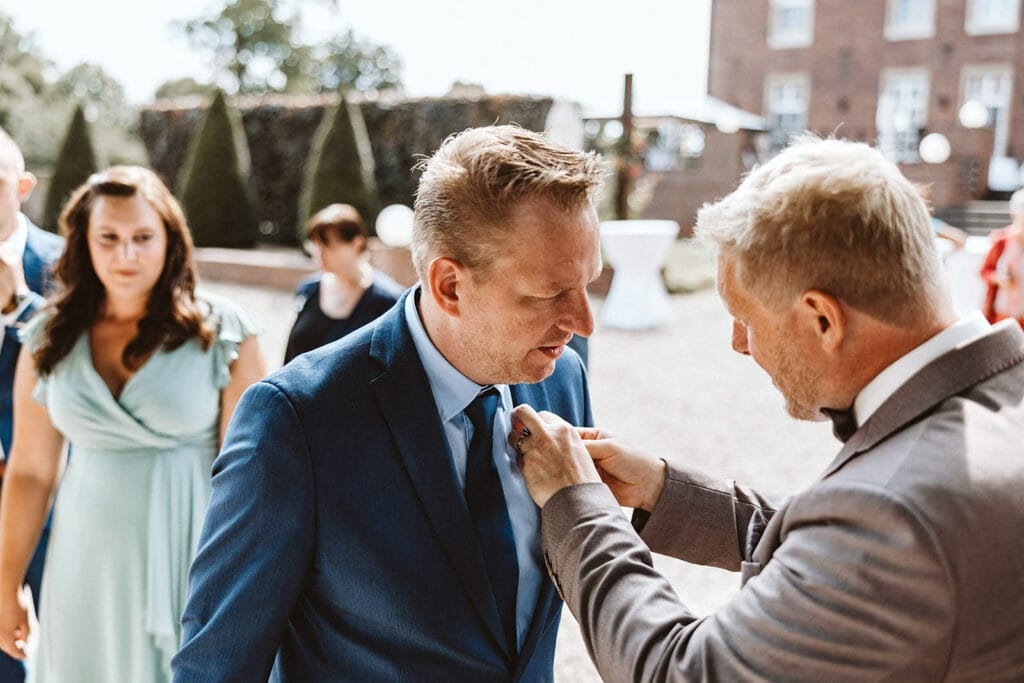 Schlosskapelle Diersfordt Wesel Schloss Diersfordt Wesel Hochzeitsfotograf - Bräutigam richtet Krawatte eines Hochzeitsgasts zurecht bei Gratulation