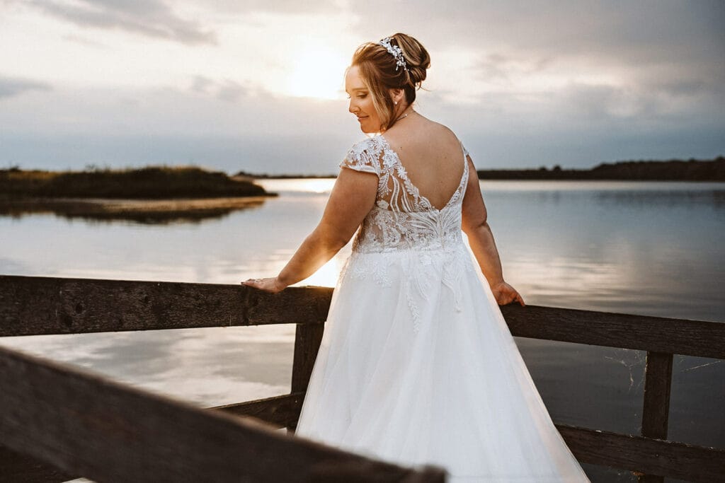 Schlosskapelle Diersfordt Wesel Schloss Diersfordt Wesel Hochzeitsfotograf - Braut steht auf Steg vor einem See. Es herrscht Sonnenuntergang