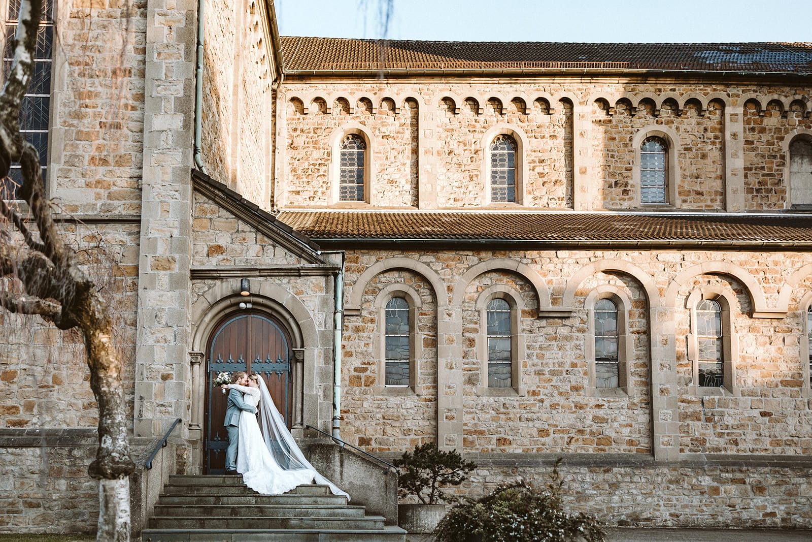 St. Mariä Empfängnis Essen Hochzeitsfotograf - Brautpaar vor dem Eingang der Kirche bei Sonnenuntergang