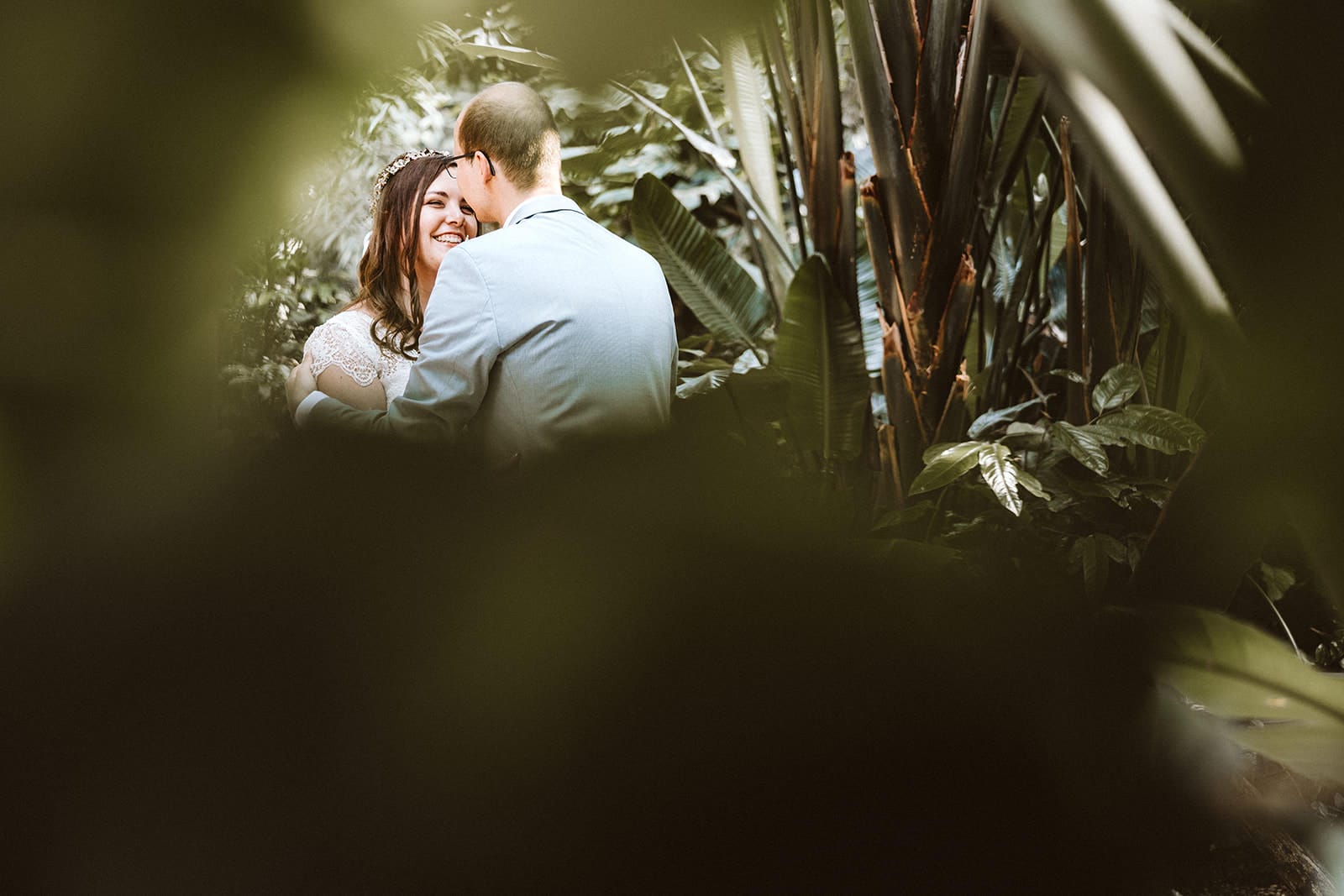ZOOM Erlebniswelt Gelsenkirchen Ryokan Gelsenkirchen Hochzeitsfotograf - Blick durch Blätter auf Brautpaar Umarmung beim Getting Ready