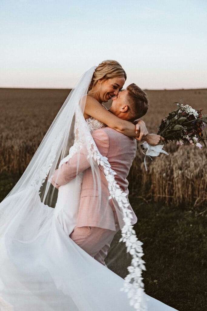 Die Farm Essen die Straußenfarm Essen Hochzeitsfotograf - Bräutigam küsst Braut und hebt sie in die Luft. Er dreht sich mit der Braut im Kreis. Der Schleier fliegt dabei
