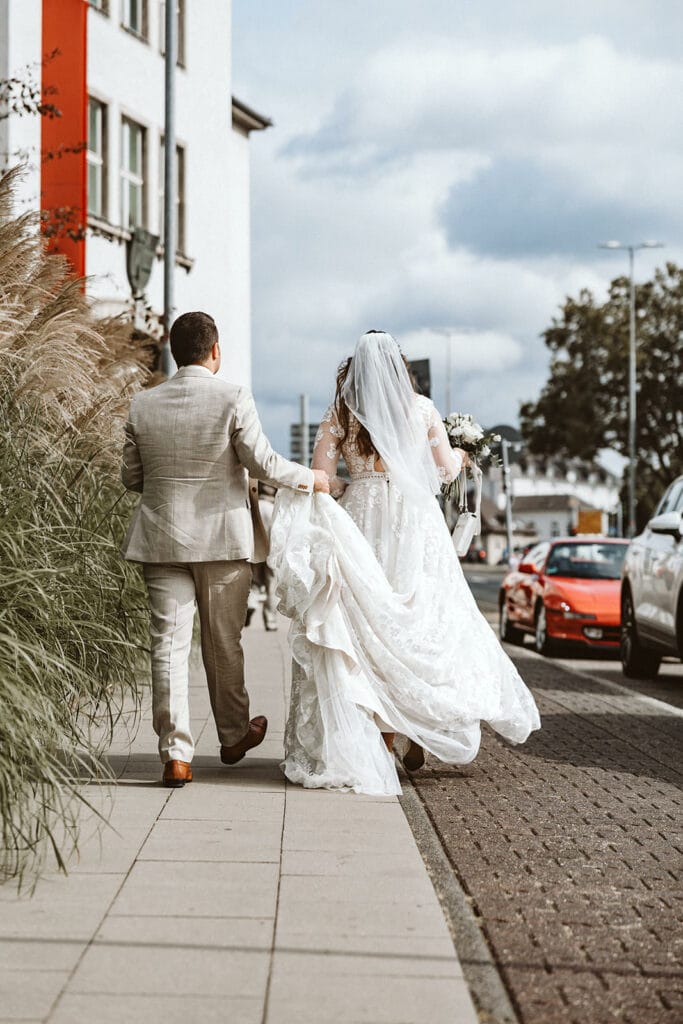 St. Marien Witten Hochzeitsfotograf - Braut und Bräutigam gehen zu rotem Auto in der Stadt