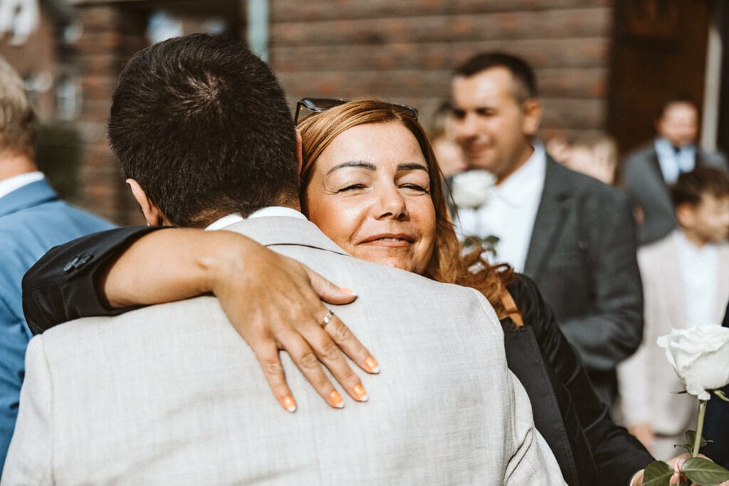 St. Marien Witten Hochzeitsfotograf - mittelalte Frau umarmt Bräutigam und beglückwünscht ihn zur Ehe