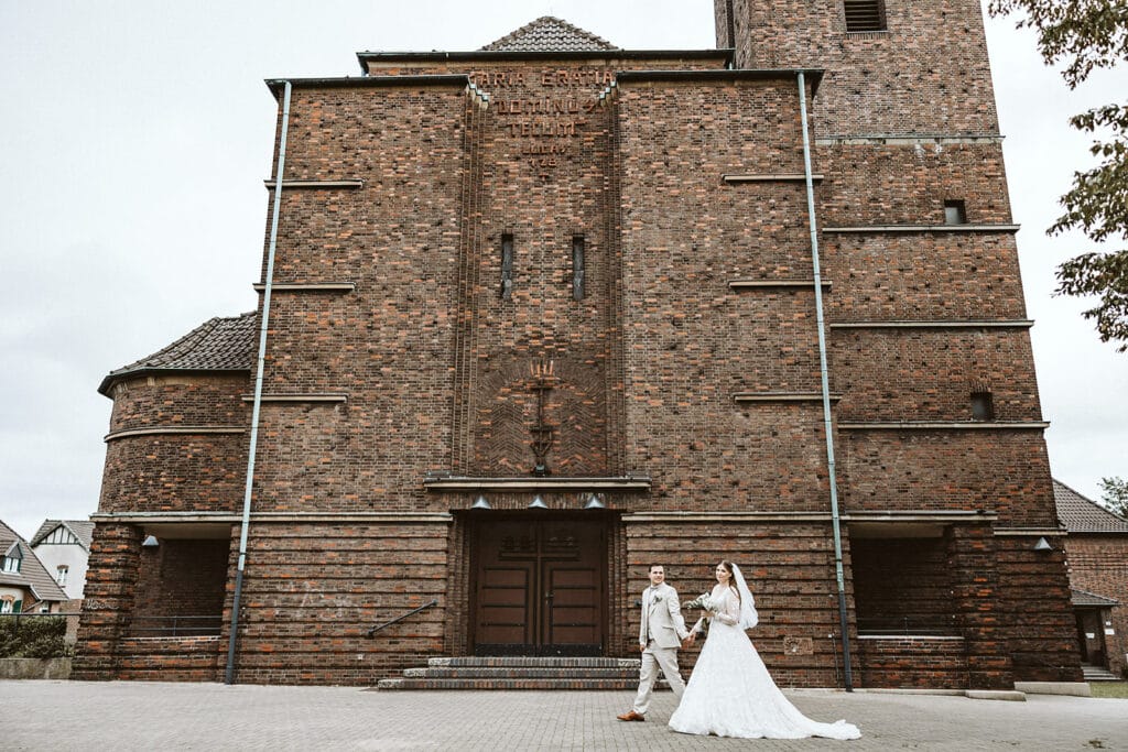 St. Marien Witten Hochzeitsfotograf - Braut und Bräutigam Brautpaar läuft hand in Hand vor Kirche