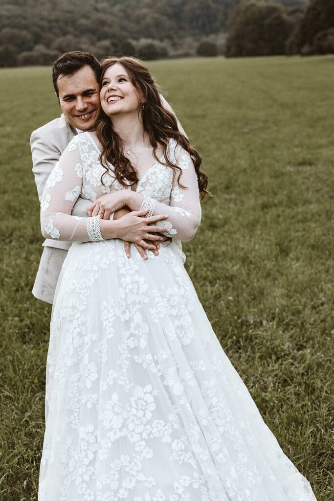 St. Marien Witten Hochzeitsfotograf - Bräutigam hält Braut von hinten Fest und lacht miteinander