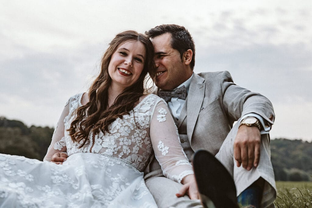 St. Marien Witten Hochzeitsfotograf - Braut und Bräutigam sitzen zusammen auf dem Wiesenboden und lächeln in die Kamera