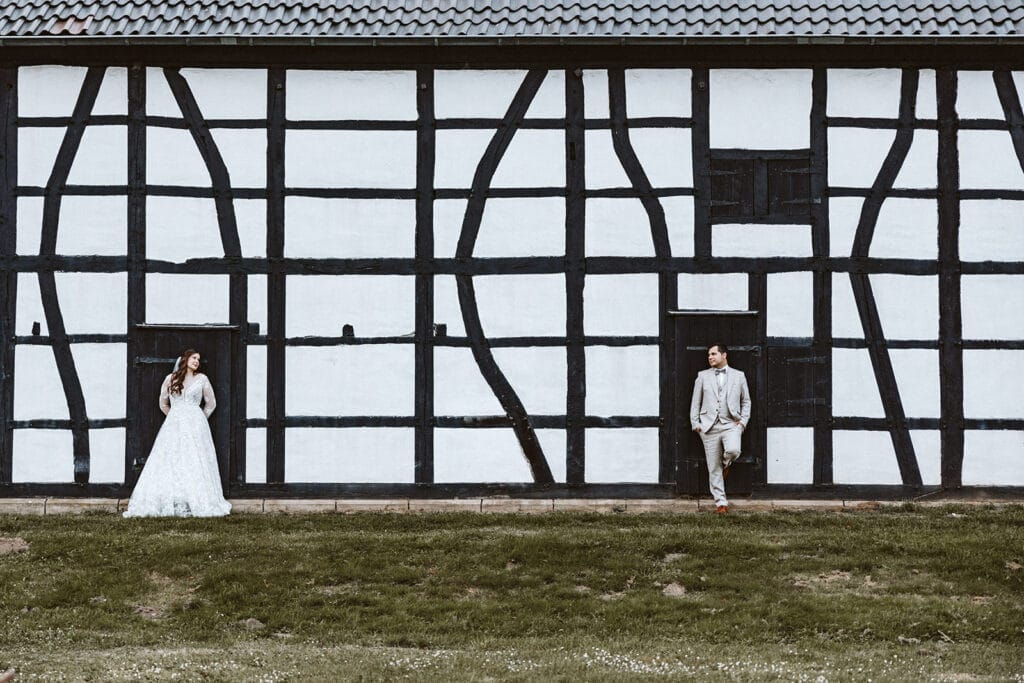 St. Marien Witten Hochzeitsfotograf - Braut und Bräutigam Brautpaar stehen vor einem Fachwerkhaus in weiß