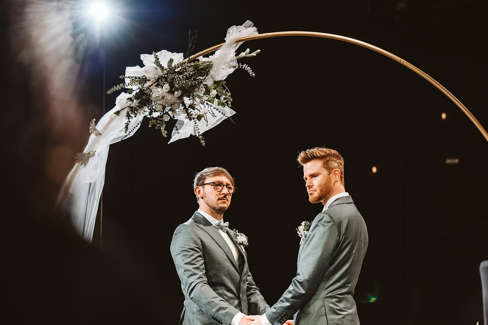 Theater Narrenschiff Unna Lindenbrauerei Kühlschiff Unna Hochzeitsfotograf - Gleichgeschlechtliches schwules Ehepaar hält sich unter Traubogen die Hände