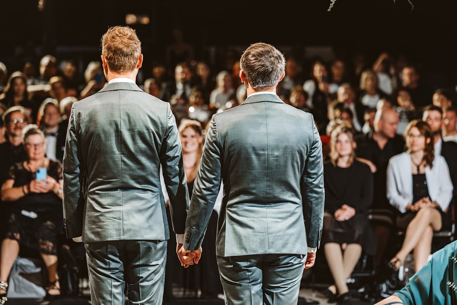 Theater Narrenschiff Unna Lindenbrauerei Kühlschiff Unna Hochzeitsfotograf - Homosexuelles, gleichgeschlechtliches schwules Ehepaar hält sich die Hände und schaut zu den Hochzeitsgästen