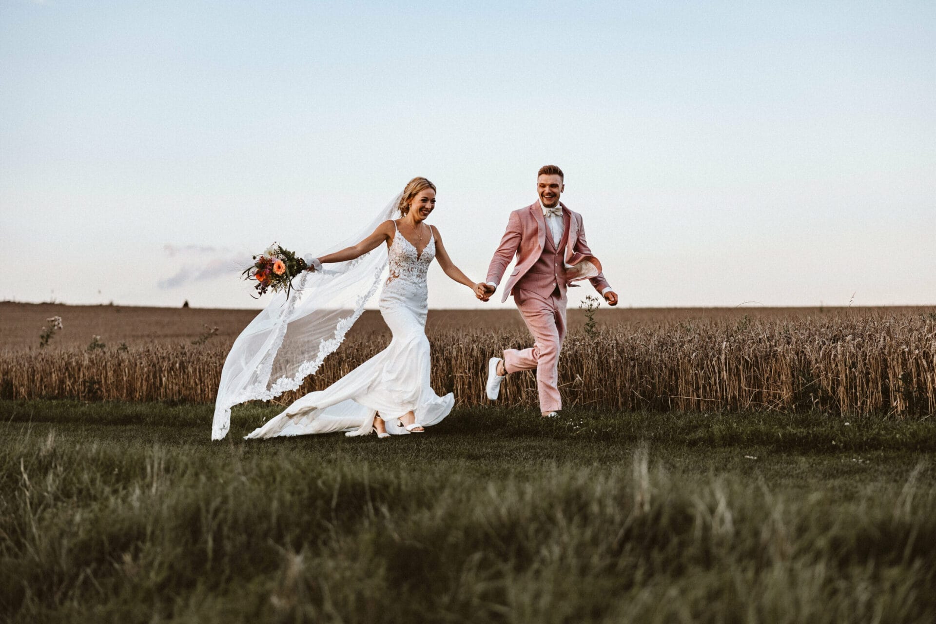 Hochzeit Heiraten Hochzeitsfotograf Dominik Neugebauer - Braut und Bräutigam halten Händchen und rennen vor einem Kornfeld