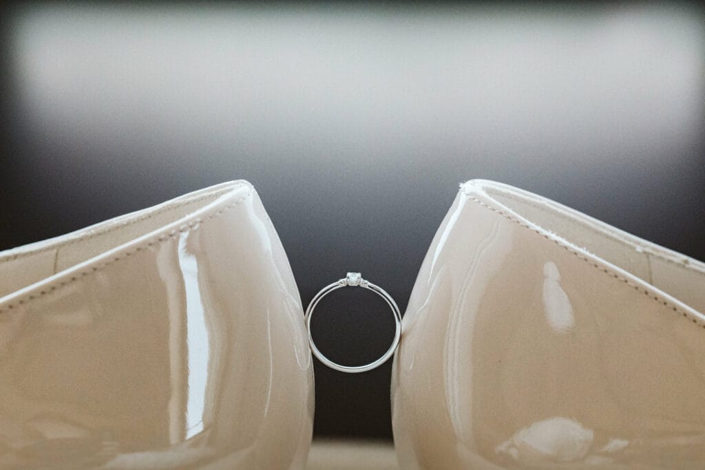 Hochzeit Heiraten Hochzeitsfotograf Dominik Neugebauer - Ein Hochzeitsring wird in der Mitte in der Luft gehalten durch zwei Brautpaarschuhe der Braut, welche gegenüberliegend stehen und den Hochzeitsring festhalten.