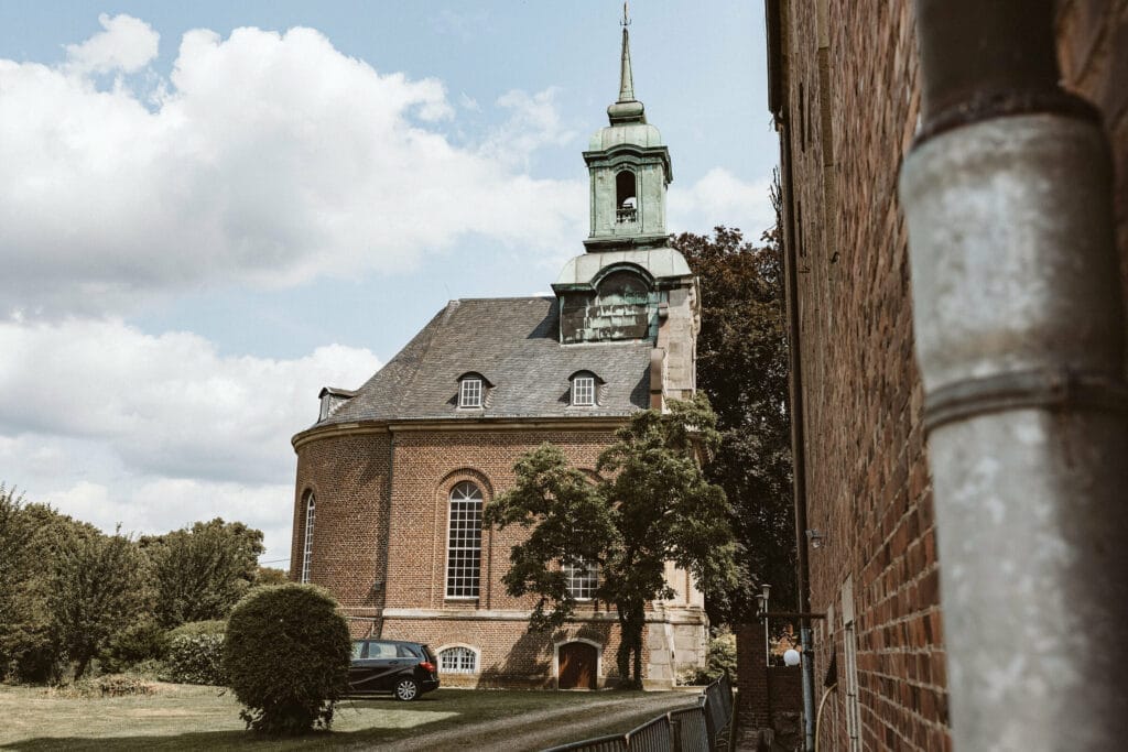 Hochzeit Heiraten Hochzeitsfotograf Dominik Neugebauer - Das Gebäude der Kapelle im Weitwinkel-Format aufgenommen. Es ist ein sonniger Tag. Nur ein paar vereinzelte Wolken sind für die Hochzeit zu erkennen.