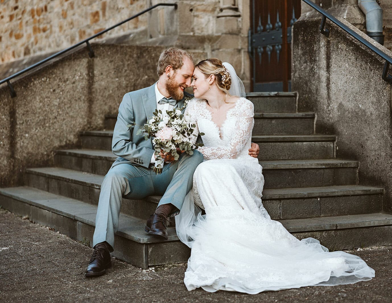 Hochzeit Heiraten Hochzeitsfotograf Dominik Neugebauer Portfolio - Braut und Bräutigam sitzen auf einer Treppe einer Kirche und umarmen sich