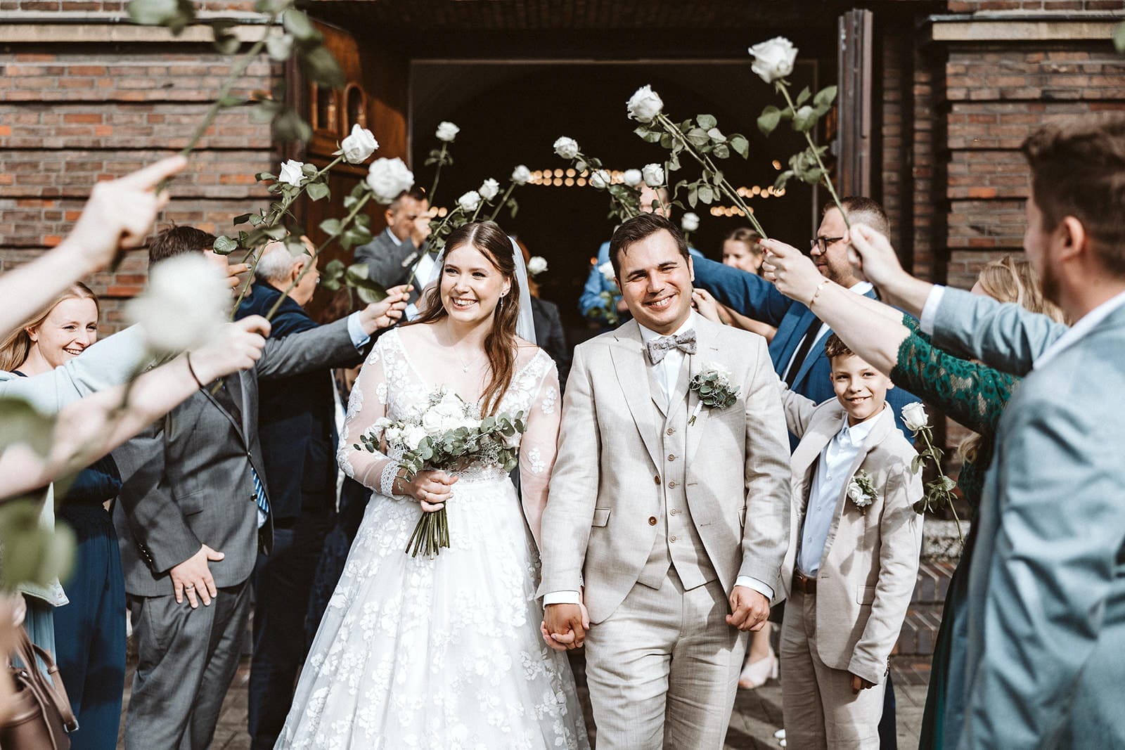 Hochzeit Heiraten Hochzeitsfotograf Dominik Neugebauer Portfolio - Brautpaar geht durch Spalier nach der kirchlichen Trauung. Hochzeitsgäste haben weiße Rosen in den Händen