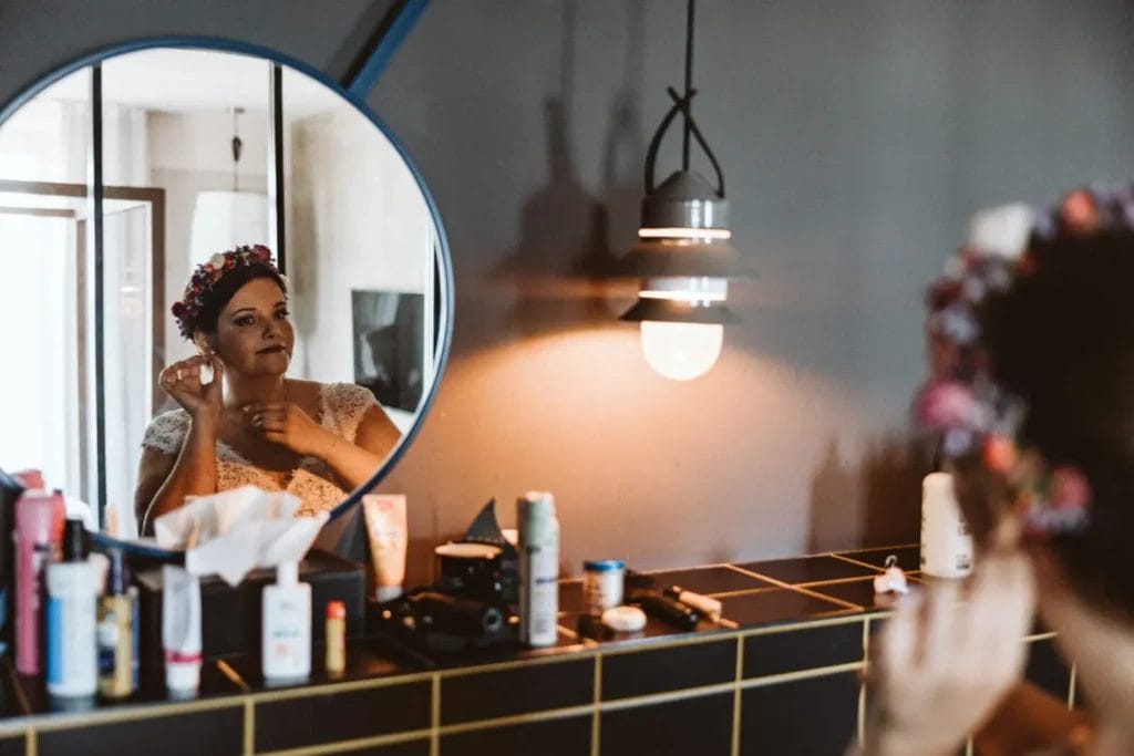 Auf der Hochzeit perfekt aussehen - Braut schaut sich in einem runden Spiegel im Badezimmer eines Hotels an