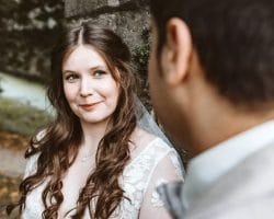 Eine Frau in einem weißen Spitzenkleid mit langen, gewellten braunen Haaren lächelt einen Mann in einem hellen Anzug herzlich an. Halten Sie diesen magischen Moment fest - Tipps Hochzeitsfotograf helfen Ihnen dabei, solche Erinnerungen für immer zu bewahren, und das in einer wunderschönen Umgebung.