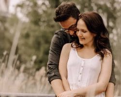 Hochzeitstraditionen vor dem großen Tag - Pärchen umarmt sich von hinten im Kornfeld und kuschelt miteinander