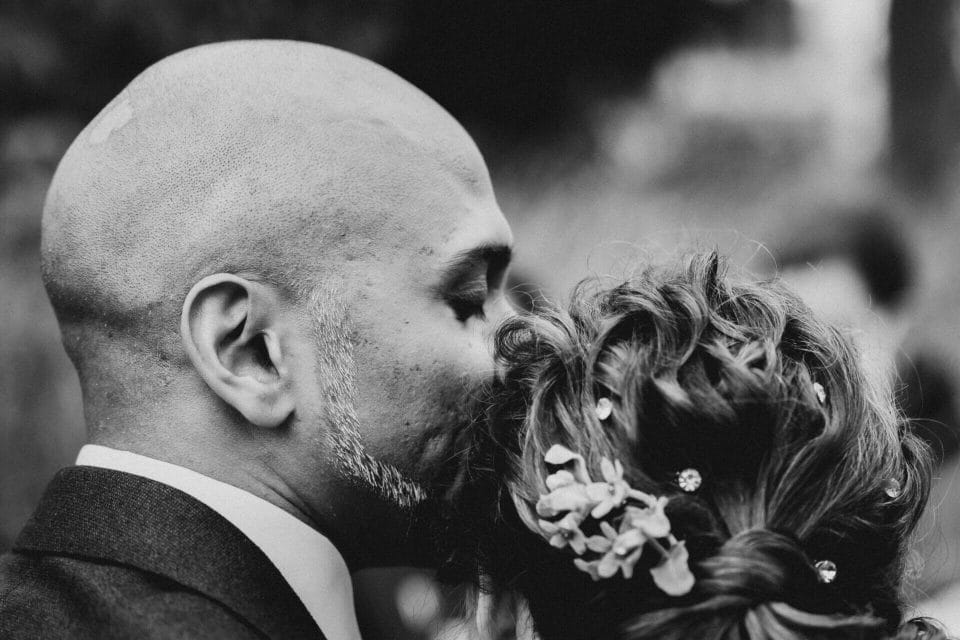 Regen am Hochzeitstag - Bräutigam küsst Braut auf den Kopf und schließt seine Augen dabei