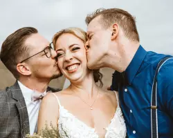 So entstehen tolle Gruppenfotos für die Hochzeit - Braut wird von Trauzeugen auf die Wange geküsst. Die Braut lächelt dabei
