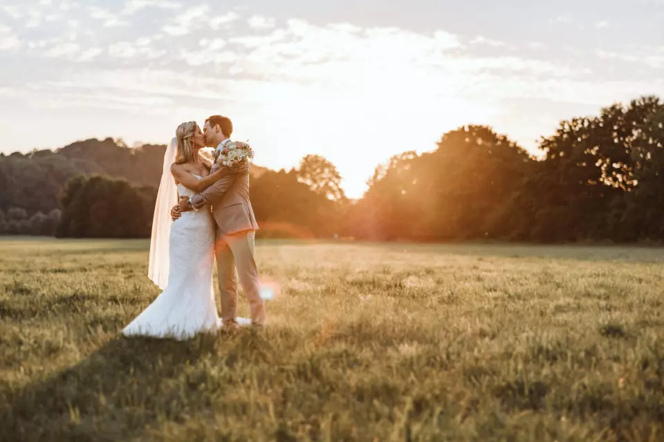 So viel kostet ein Hochzeitsfotograf - Preise und Kosten für Hochzeitsfotos und anderen Dienstleistungen - Brautpaar steht im Abendlicht zum Sonnenuntergang auf einem Feld