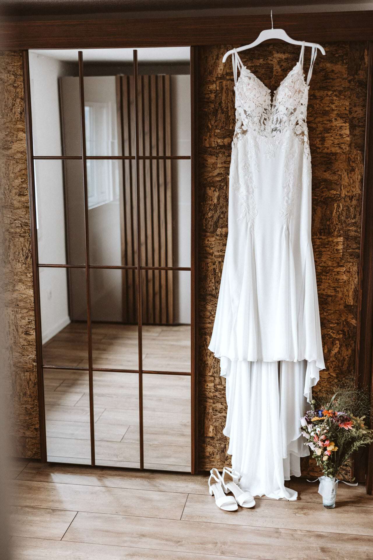 Hochzeitsfotograf Bochum Hochzeit Heiraten Hochzeitsfotos - Hochzeitskleid hängt auf einem weißen Kleiderbügel neben einem Spiegel. Unter dem Hochzeitskleid ist ein Blumenstrauß und Schuhe zu sehen