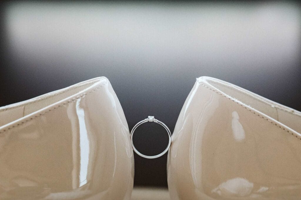 Hochzeitsfotograf Remscheid Hochzeit Heiraten Hochzeitsfotos - Ein Hochzeitsring wird in der Mitte in der Luft gehalten durch zwei Brautpaarschuhe der Braut, welche gegenüberliegend stehen und den Hochzeitsring festhalten