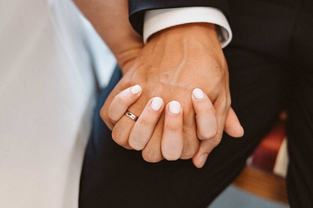 Hochzeitsfotograf Remscheid Hochzeit Heiraten Hochzeitsfotos - Detailaufnahme von den verschlungenen Händen zwischen Braut und Bräutigam nach der Ringübergabe. Der Hochzeitsring des Bräutigams ist dabei zu erkennen