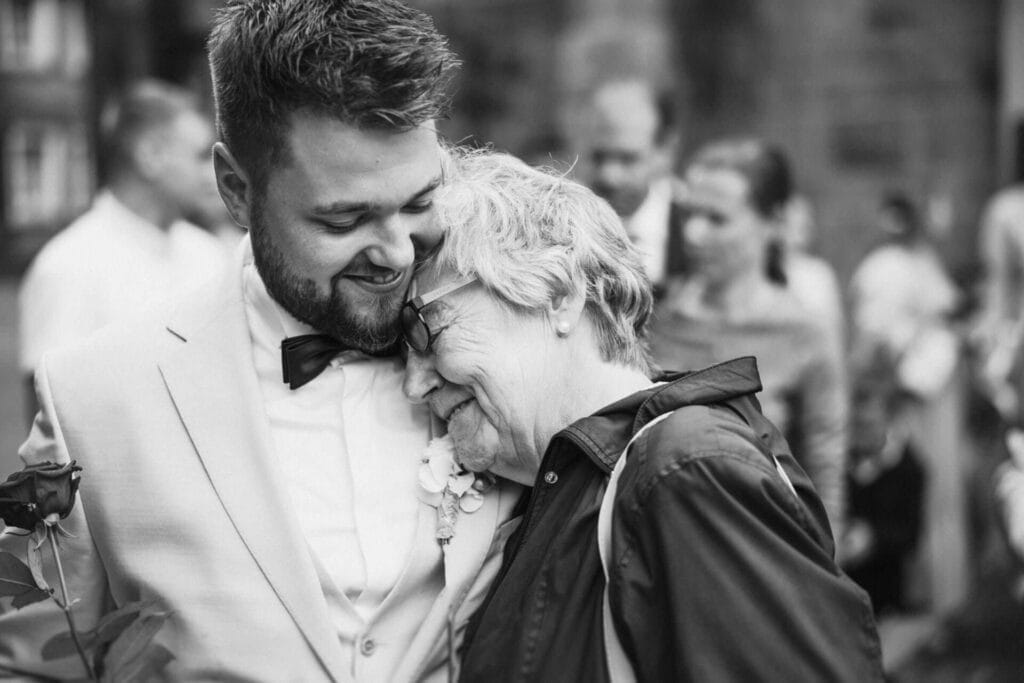 Hochzeitsfotograf Remscheid Hochzeit Heiraten Hochzeitsfotos - Die Großmutter beziehungsweise die Oma lehnt sich an den Bräutigam seiner Schulter an. Beide lächeln sehr liebevoll miteinander und feiern den Moment