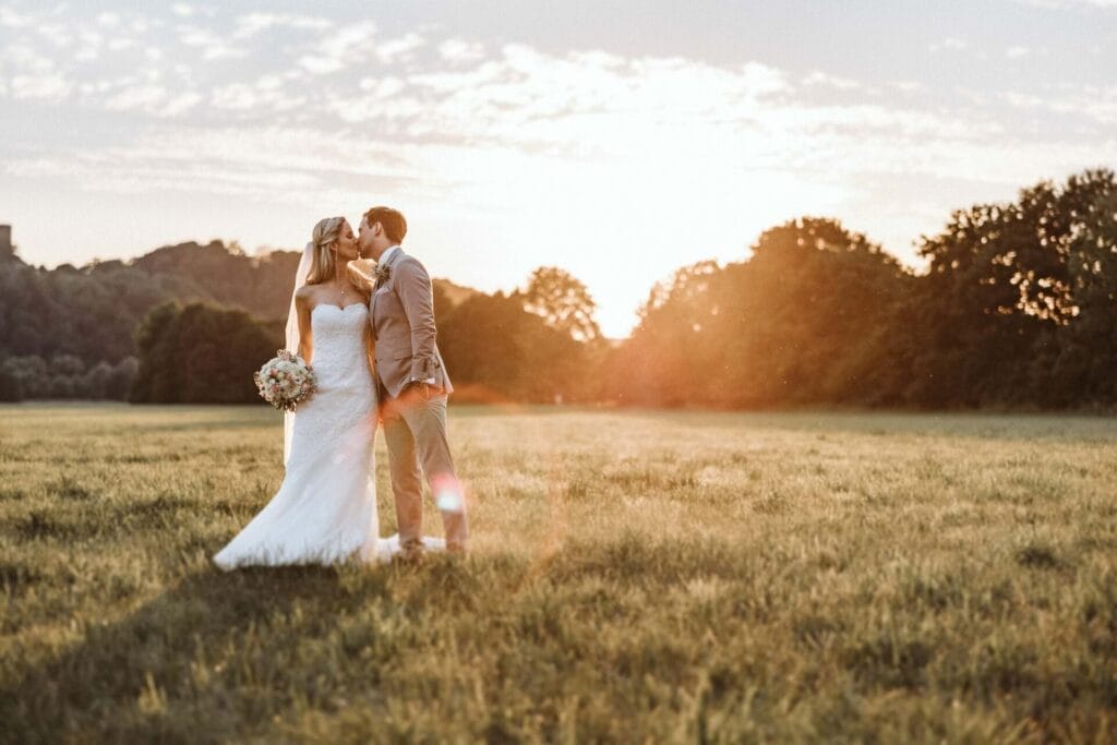 Hochzeitsfotograf Remscheid Hochzeit Heiraten Hochzeitsfotos - Braut und Bräutigam küssen sich auf dem Feld. Es ist die Abendsonne zu erkennen