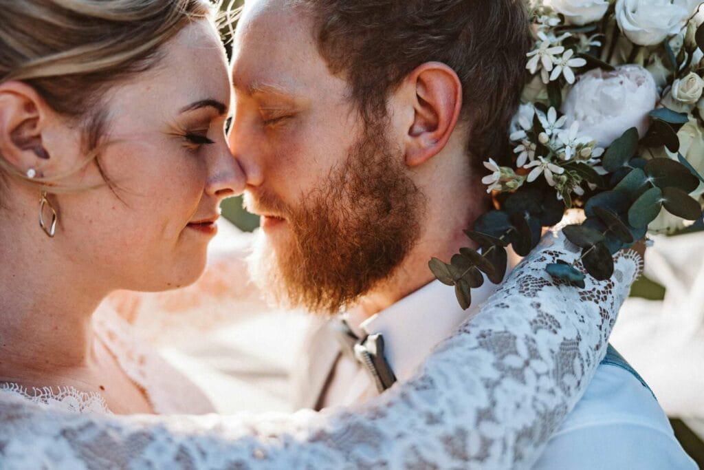 Hochzeitsfotograf Remscheid Hochzeit Heiraten Hochzeitsfotos - Braut und Bräutigam reiben sich mit ihren Nasen aneinander. Beide haben die Augen geschlossen und genießen den Moment. Die Braut legt ihre Arme um den Hals des Bräutigams. Sie hält dabei den Brautstrauß fest. Zwischen ihren Gesichtern spitzt die Abendsonne hervor