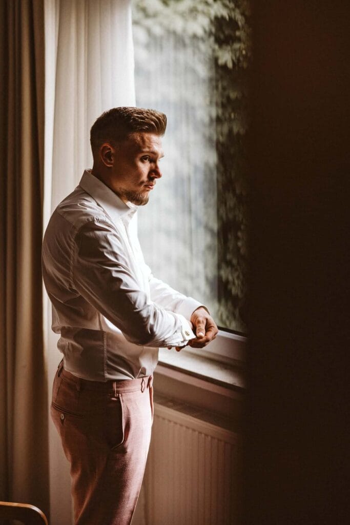 Hochzeitsfotograf Duisburg Hochzeit Heiraten Hochzeitsfotos - Der Bräutigam schaut aus dem Fenster. Er knöpft sich die Manschettenknöpfe an und schließt den Ärmel des Hemdes