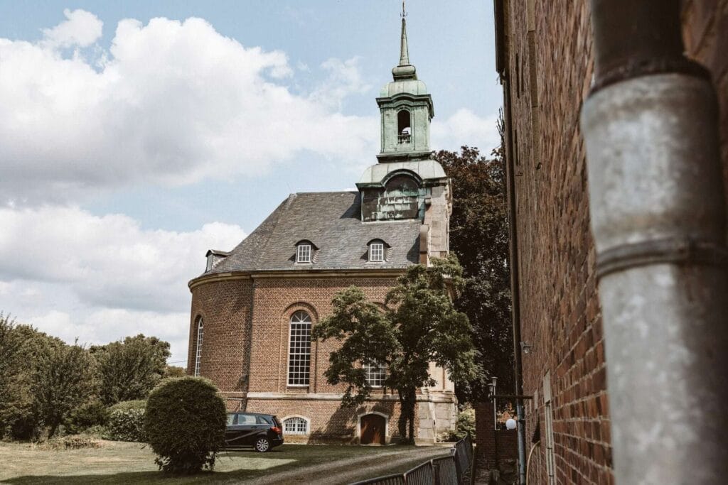 Hochzeitsfotograf Duisburg Hochzeit Heiraten Hochzeitsfotos - Das Gebäude der Kapelle im Weitwinkel-Format aufgenommen. Es ist ein sonniger Tag. Nur ein paar vereinzelte Wolken sind für die Hochzeit zu erkennen