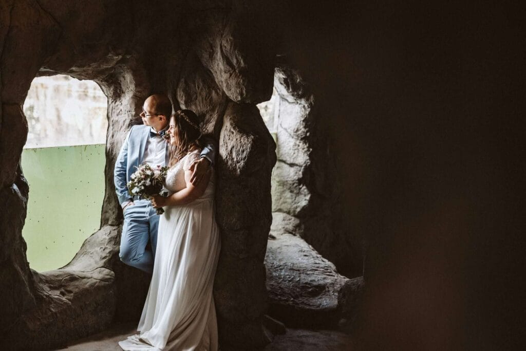 Hochzeitsfotograf Duisburg Hochzeit Heiraten Hochzeitsfotos - Braut und Bräutigam sehen aus einem Fenster in die Ferne. Sie befinden sich in einer gestalteten Höhle. Das Fenster ist ein Sichtschutz, um Tiere zu erkennen, die sich im Wasser bewegen