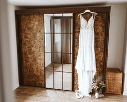 Pro und Contra für das Mieten eines Hochzeitskleides - Weißes Hochzeitskleid hängt vor einer Wand. Nebendran ein Spiegel.