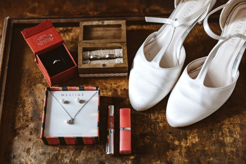 Hochzeitsfotograf Dorsten Hochzeit Heiraten Hochzeitsfotos - Neben dem Verlobungsring und den beiden Hochzeitsringen sind die beiden Brautschuhe zu erkennen. Weiterhin sind auf dem Bild Ohrringe, eine Kette für die Hochzeit sowie Lippenstift und Eyeliner zu erkennen
