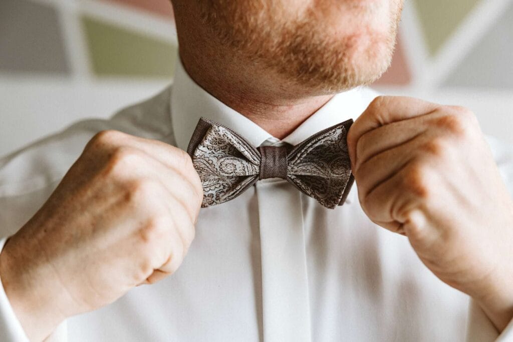 Hochzeitsfotograf Dorsten Hochzeit Heiraten Hochzeitsfotos - Der Bräutigam bindet sich eine Fliege an sein Hemd. Die Fliege hat die Farben braun, hellbraun beige sowie weiß