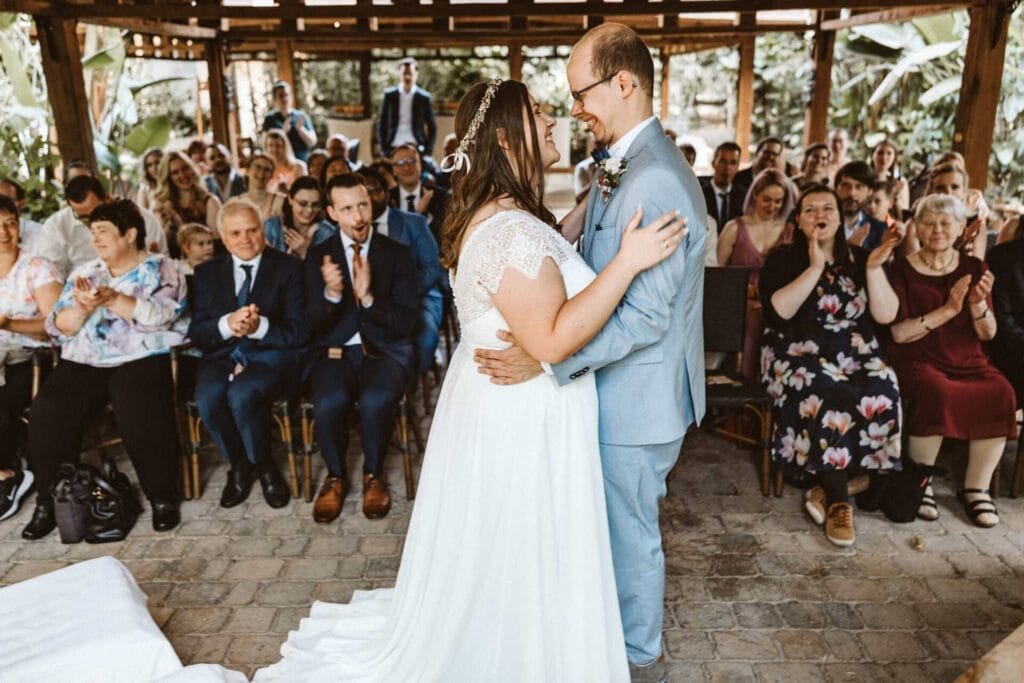 Hochzeitsfotograf Schwerte Hochzeit Heiraten Hochzeitsfotos - Braut und Bräutigam gehen Hand in Hand und mit lächelndem Gesichtsausdruck durch das Spalier der Hochzeitsgäste. Die Hochzeitsgäste bejubeln das frisch getraute Brautpaar