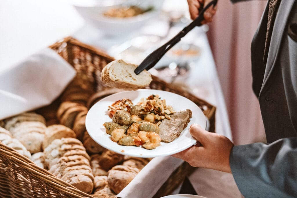 Was Euch niemand über Euren großen Tag verrät - Gast legt sich Essen auf den Teller und greift nach einer Brotscheibe Dinner Catering