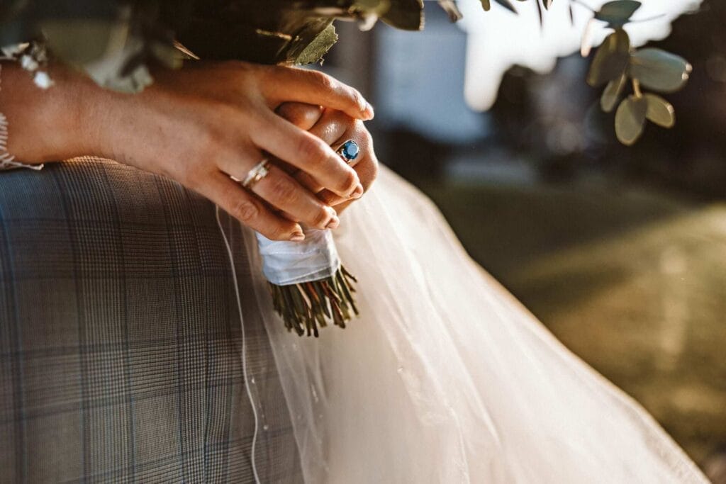 Hochzeitsfotograf Hardecke Hochzeit Heiraten Hochzeitsfotos - Ein blauer Ring und der Hochzeitsring bei der Braut sind zu erkennen, während sie den Bräutigam umarmt. Sie hält den Blumenstrauß fest. Es ist eine Detailaufnahme