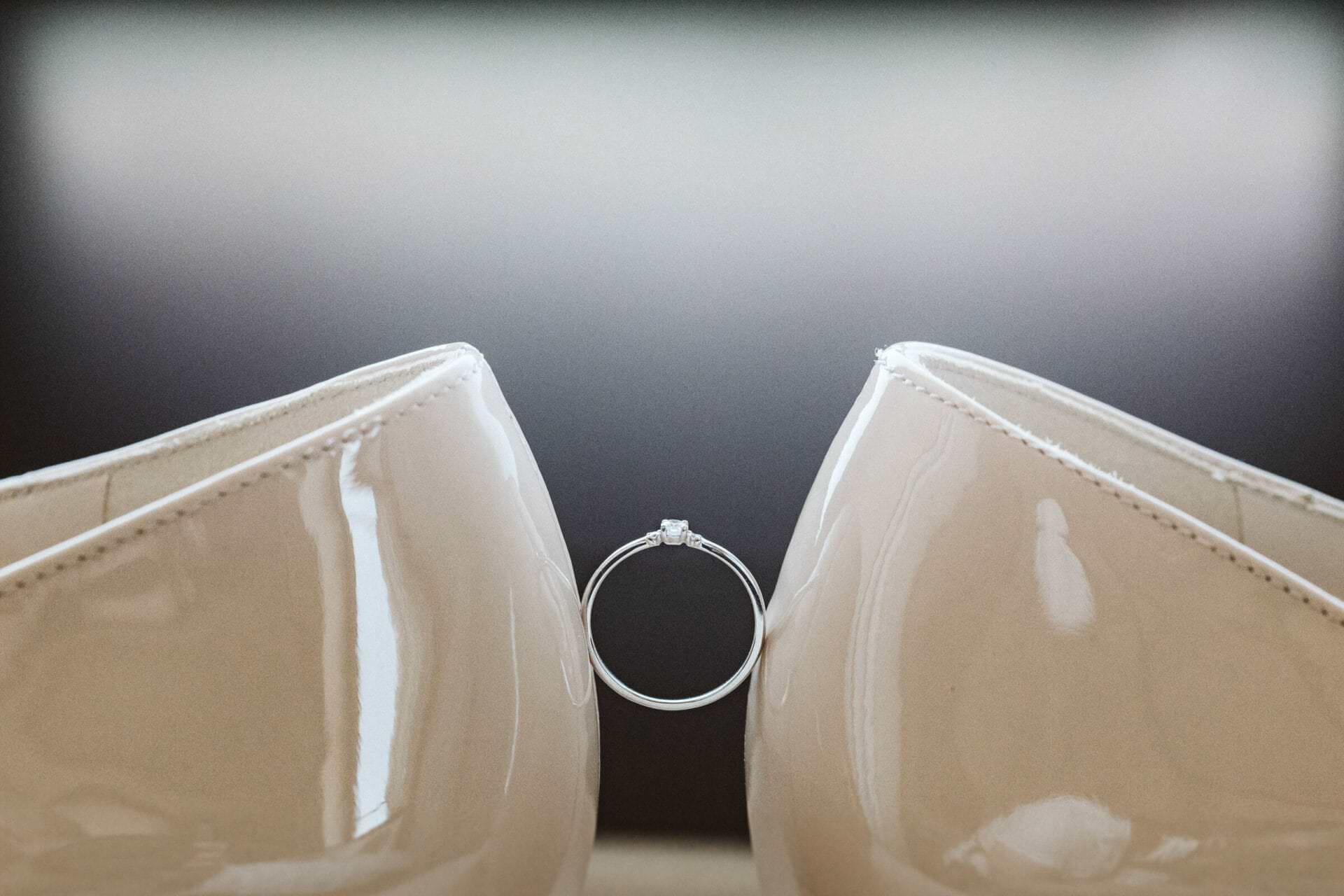 Hochzeitsfotograf Herten Hochzeit Heiraten Hochzeitsfotos - Ein Hochzeitsring wird in der Mitte in der Luft gehalten durch zwei Brautpaarschuhe der Braut, welche gegenüberliegend stehen und den Hochzeitsring festhalten