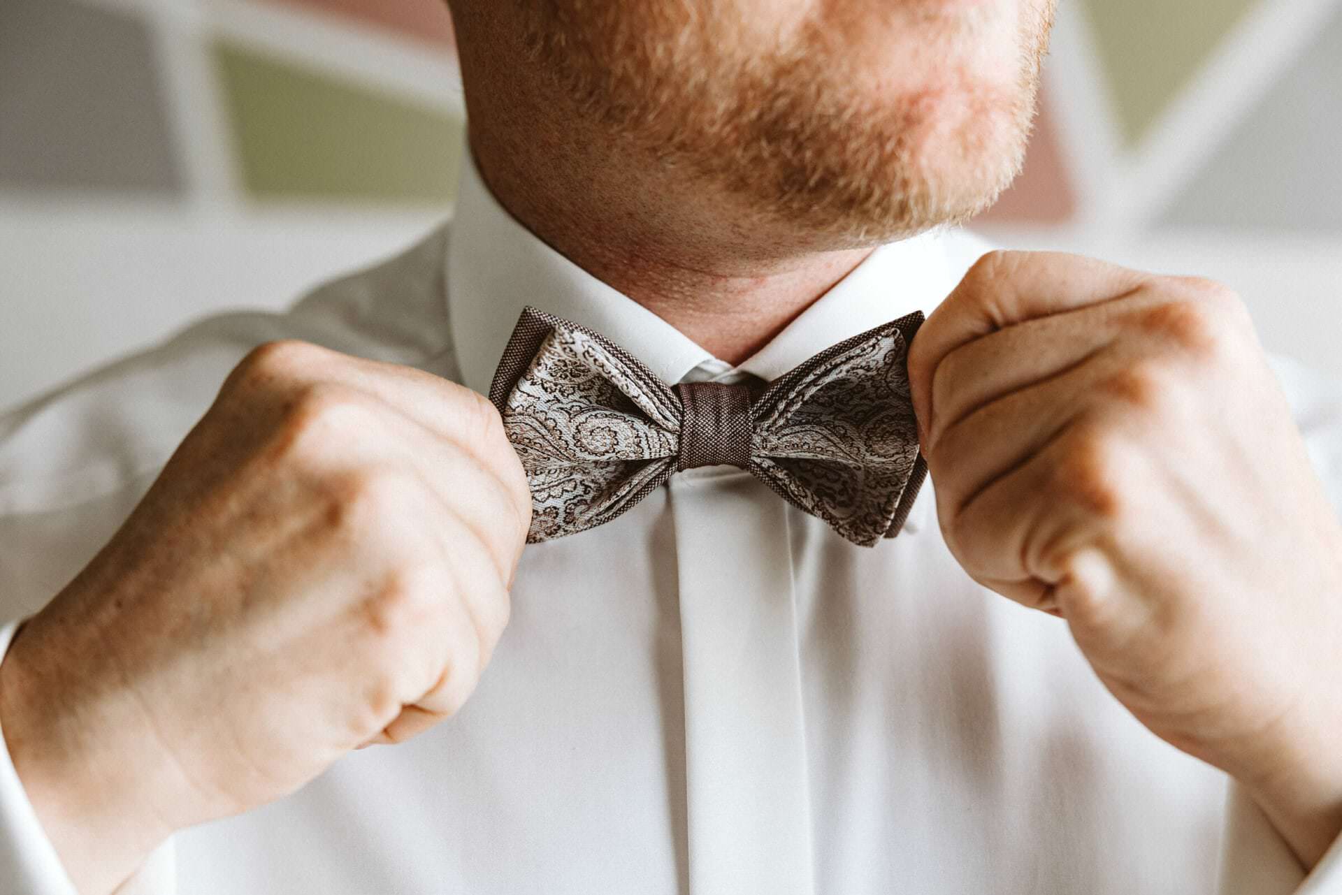 Hochzeitsfotograf Herten Hochzeit Heiraten Hochzeitsfotos - Der Bräutigam bindet sich eine Fliege an sein Hemd. Die Fliege hat die Farben braun, hellbraun beige sowie weiß