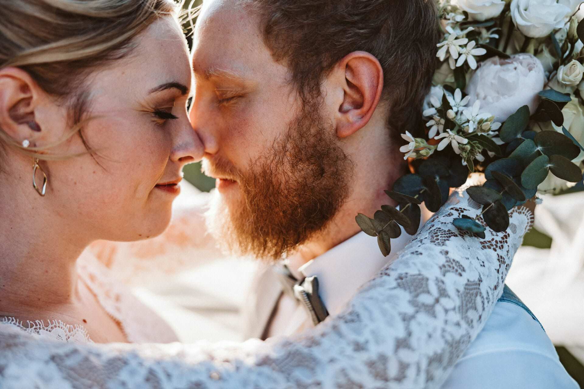 Hochzeitsfotograf Krefeld Hochzeit Heiraten Hochzeitsfotos - Braut und Bräutigam reiben sich mit ihren Nasen aneinander. Beide haben die Augen geschlossen und genießen den Moment. Die Braut legt ihre Arme um den Hals des Bräutigams. Sie hält dabei den Brautstrauß fest. Zwischen ihren Gesichtern spitzt die Abendsonne hervor