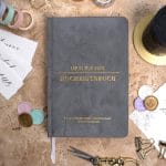 Mein kleines Hochzeitsbuch Hochzeitsplaner Wedding Planner Grau - Flatlay-Ansicht des Hochzeitsplaners auf einem braunen, dekorierten Tisch mit Accessoires, Wachssiegel, Hochzeitseinladung, Kerze