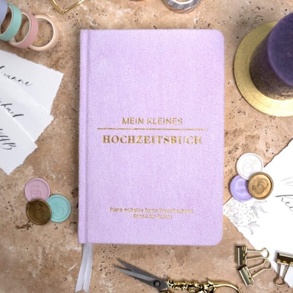Mein kleines Hochzeitsbuch Hochzeitsplaner Wedding Planner Lila - Flatlay-Ansicht des Hochzeitsplaners auf einem braunen, dekorierten Tisch mit Accessoires, Wachssiegel, Hochzeitseinladung, Kerze