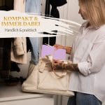 Mein kleines Hochzeitsbuch Hochzeitsplaner Wedding Planner Lila - Kompakt und immer dabei - handlich und praktisch - Zukünftige Braut packt Hochzeitsplaner Wedding Planner in die Handtasche vor einer Garderobe